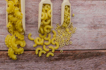 Dried pasta food selection in wooden spoons over old oak background.の写真素材