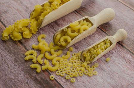 Dried pasta food selection in wooden spoons over old oak background.の写真素材