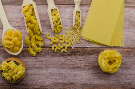 Dried pasta food selection in wooden spoons over old oak background.の写真素材