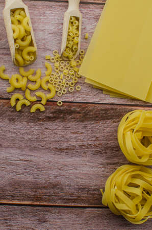Dried pasta food selection in wooden spoons over old oak background.の写真素材