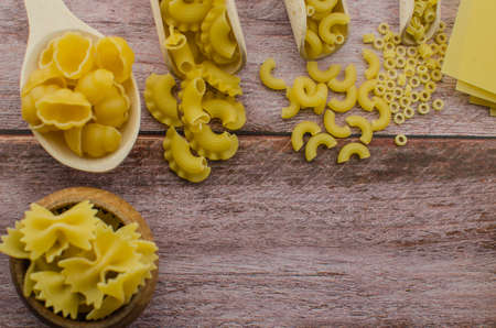 Dried pasta food selection in wooden spoons over old oak background.の写真素材