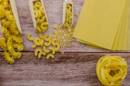 Dried pasta food selection in wooden spoons over old oak background.の写真素材
