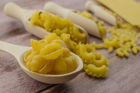 Dried pasta food selection in wooden spoons over old oak background.の写真素材