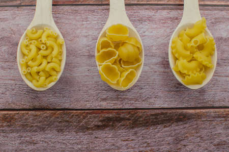 Dried pasta food selection in wooden spoons over old oak background.の写真素材