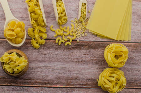 Dried pasta food selection in wooden spoons over old oak background.の写真素材