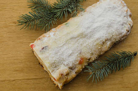 Christmas stollen on darkfestive background with fir twigs, lights and and berries. Close-up on this traditional German dessert for Christmas celebration.の写真素材