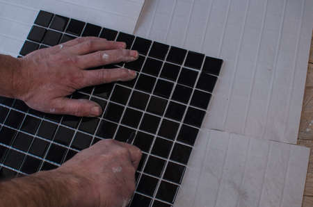 Home repair: installing the mosaic tile on the wall. A worker covers the wall with adhesive using a notched trowel.の写真素材