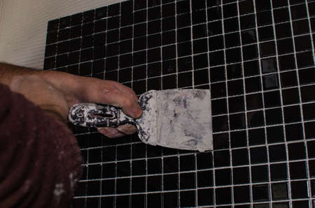 Home repair: installing the mosaic tile on the wall. A worker covers the wall with adhesive using a notched trowel.の写真素材