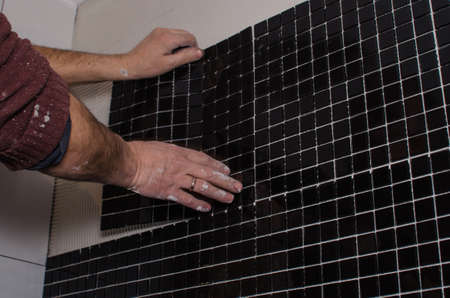 Home repair: installing the mosaic tile on the wall. A worker covers the wall with adhesive using a notched trowel.の写真素材