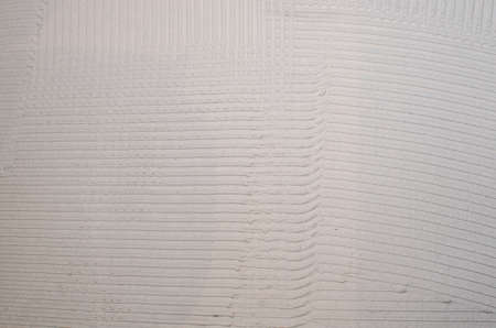 Home repair: installing the mosaic tile on the wall. A worker covers the wall with adhesive using a notched trowel.の写真素材