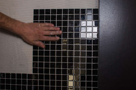 Home repair: installing the mosaic tile on the wall. A worker covers the wall with adhesive using a notched trowel.の写真素材