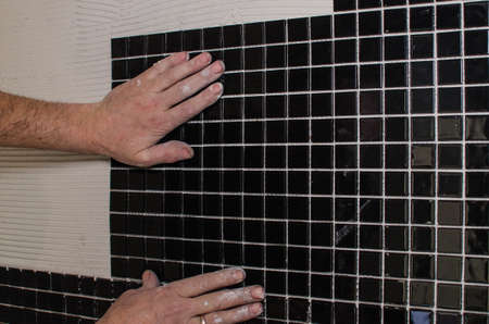 Home repair: installing the mosaic tile on the wall. A worker covers the wall with adhesive using a notched trowel.の写真素材