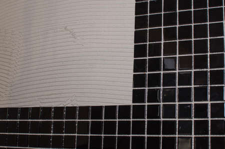 Home repair: installing the mosaic tile on the wall. A worker covers the wall with adhesive using a notched trowel.の写真素材