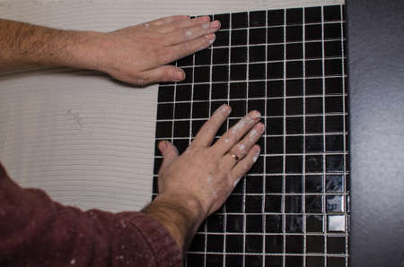 Home repair: installing the mosaic tile on the wall. A worker covers the wall with adhesive using a notched trowel.の写真素材