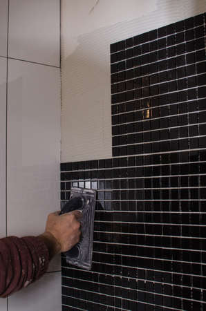 Home repair: installing the mosaic tile on the wall. A worker covers the wall with adhesive using a notched trowel.の写真素材