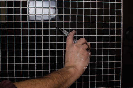 Home repair: installing the mosaic tile on the wall. A worker covers the wall with adhesive using a notched trowel.の写真素材