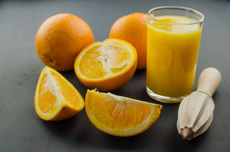 Orange juice and orang with a wooden orange juicer on a black backgroundの写真素材