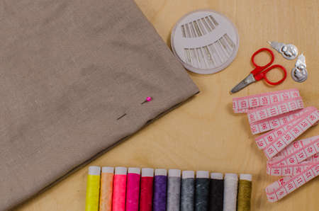 Sewing accessories. Spools of thread with different colors of rainbow, scissors, buttons, measuring tape and accessories for needlework on wooden background.の写真素材