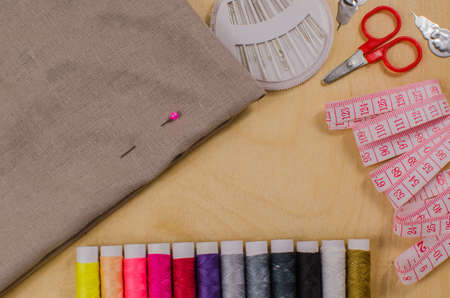 Sewing accessories. Spools of thread with different colors of rainbow, scissors, buttons, measuring tape and accessories for needlework on wooden background.の写真素材