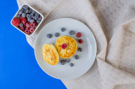 Cheese pancakes with frozen strawberries, raspberries, blueberries on a blue background. Copyspace for textの写真素材