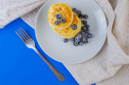 Cheese pancakes with frozen strawberries, raspberries, blueberries on a blue background. Copyspace for textの写真素材