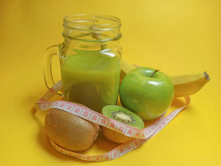 Green healthy smoothie in glass jar: banana, kiwi, green apple. Healthy drink on yellow background. Copy space for textの写真素材