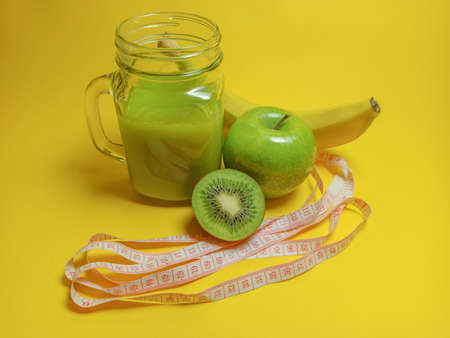 Green healthy smoothie in glass jar: banana, kiwi, green apple. Healthy drink on yellow background. Copy space for textの写真素材