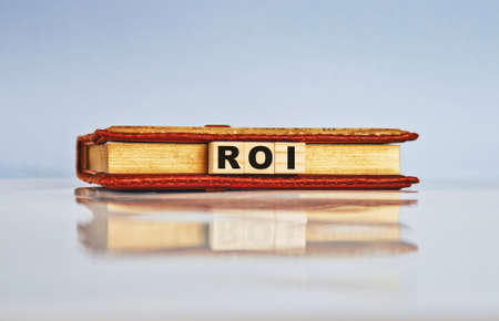 Return on Investment ROI is the concept of investing in a resource that benefits the investor. Wooden cubes with notepad and keywords.の写真素材