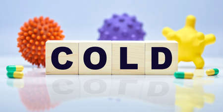COLD inscription on wooden cubes on the background of pills and toy virus. The concept of medicine.の写真素材