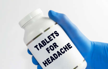 TABLETS FOR HEADACHE inscription on medicine bottles. Close-up hand of a doctor holding a vial.の写真素材