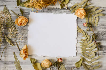 Vintage floral frame with fern leaves, dried roses flowers and branches on rustic white wooden background. Top view point. Border background vintage mock upの写真素材