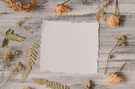 Vintage floral frame with fern leaves, dried roses flowers and branches on rustic white wooden background. Top view point. Border background vintage mock upの写真素材