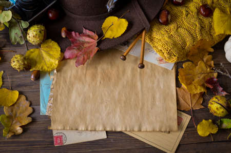 Vintage autumn frame with yellow leaves, chestnuts, hat, camera, knitting needles and retro envelopes on rustic wooden background. Top view point.の写真素材