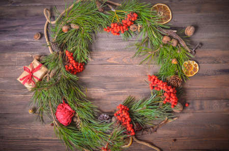 Christmas and New Year Decoration with Wreath of Pine Branches and Rowan, Orange Slices, Gift Box, Fir Cones on a Rustic Wooden Backgroundの写真素材