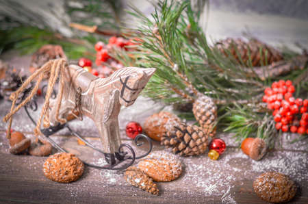 Christmas and New Year Decoration with Vintage Wooden Horse, Pine Branches, Oatmeal Cookies, Rowan, Walnuts, Fir Cones, on a Rustic Wooden Tableの写真素材