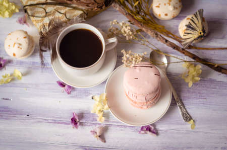 A cup of morning coffee with macaroons, butterfly, dried flowers protea and alarm clock on blurry background. Selective focus, morning breakfast still lifeの写真素材
