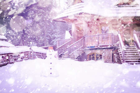 Winter wooden house and snowman in the yardの写真素材