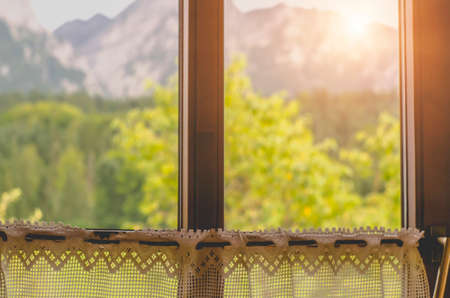 Wooden window with curtain and blurry landscape of mountains and woods behind.の写真素材