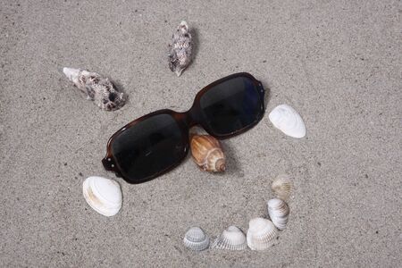 sunglasses and seashells forming a smiling face in the sandの写真素材