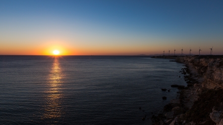 wind turbines generating clean power with lighthouse at sunsetの写真素材