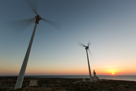 wind turbines generating clean power with lighthouse at sunsetの写真素材
