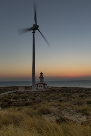 wind turbines generating clean power with lighthouse at blue hoursの写真素材