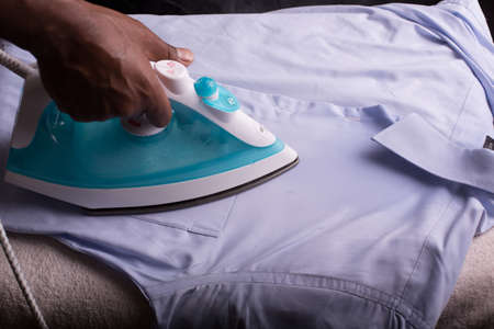 A person ironing a shirt with a steaming hot electric ironの写真素材