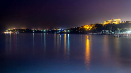 The still waters of the Atlantic ocean reflecting the colourful lights along the shores of downtown Dakarの写真素材