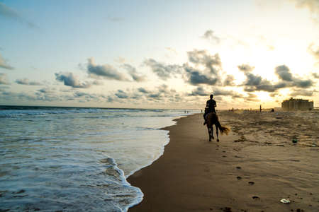 Silhouette of a man riding a horse on the shores of Obama Beach in Cotonou, Beninの写真素材