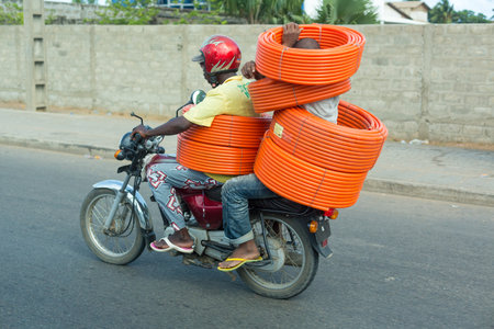 Cotonou, Benin: May 26: A man and a motorcycle taxi operator ride carrying several rolls of garden hose on May 26, 2015 in Cotonou, Benin.のeditorial素材