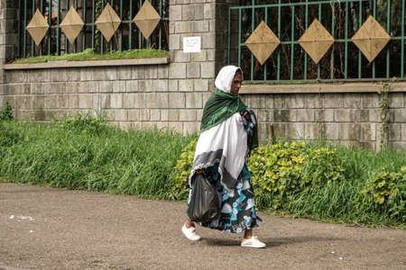 Addis Ababa - July 26: An older woman wearing a mix of modern and traditional clothing returns from the market carrying her groceries in a plastic bag on June 26, 2015 in Addis Ababa, Ethiopia.のeditorial素材