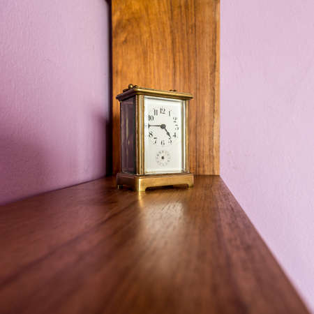 An old desk top clock with analog hour and minute hand on a shelfの写真素材