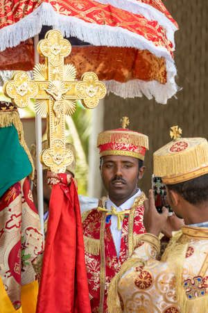 Addis Ababa - Jan 19: A priest wearing a colorful traditional gown holding a large cross has his picture taken by another priels, during a Timket celebrations of Epiphany, on January 19, 2017 in Addis Ababa, Ethiopia.のeditorial素材