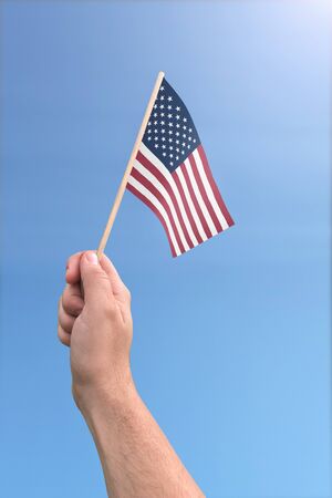 United States flag held by a hand in front of a sunny blue skyの写真素材